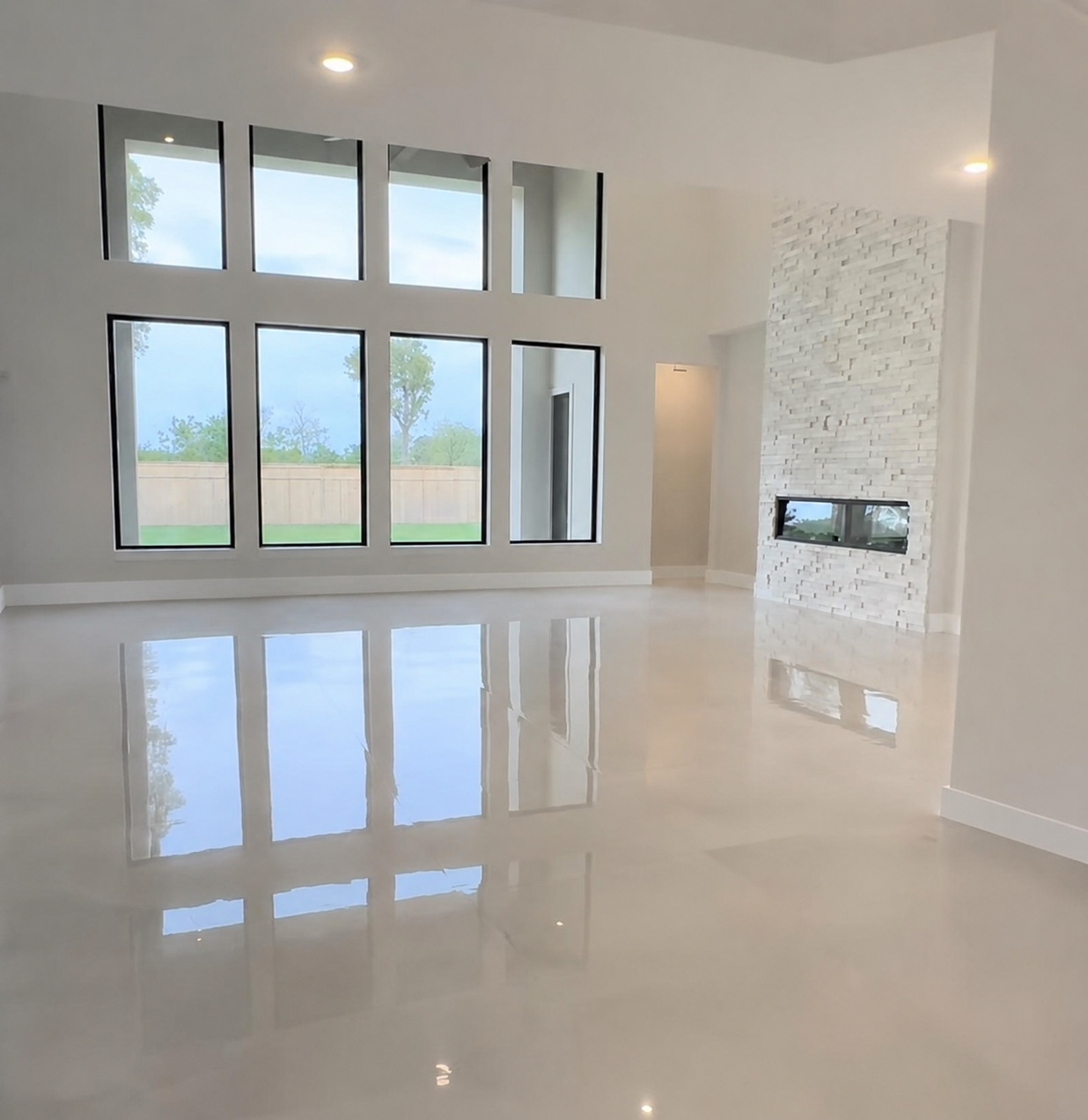 Sala luminosa con piso brillante, ventanales altos y chimenea de piedra