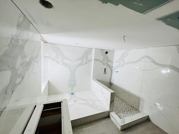 Baño en construcción con revestimiento blanco de vetas grises y ducha con mosaicos