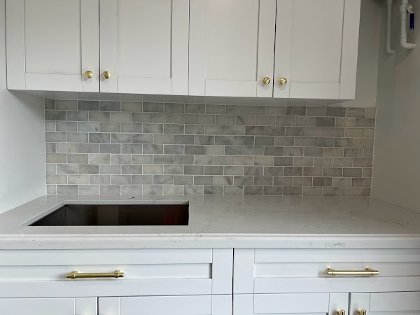 Cocina blanca con backsplash de piezas rectangulares grises y manijas doradas