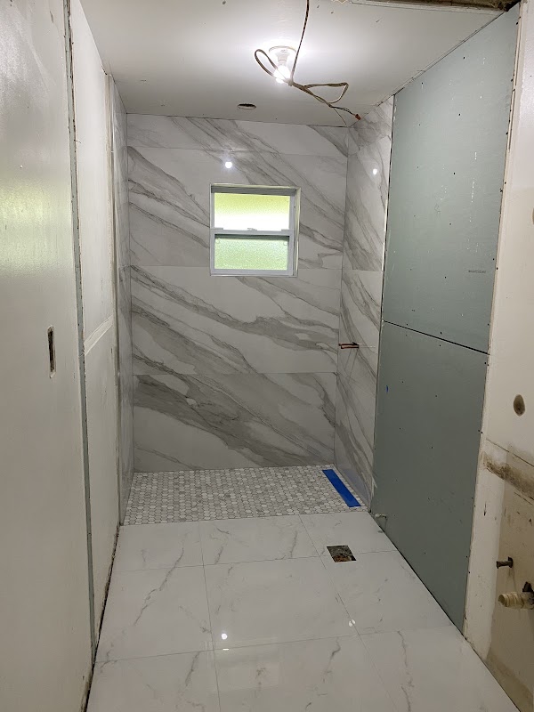 Ducha en construcción con revestimiento blanco de vetas grises y piso de mosaico